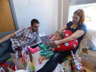 Sophie: Family sit on bed while opening presents