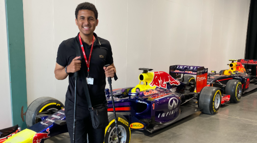 Zac standing and smiling in front of a series of race cars.