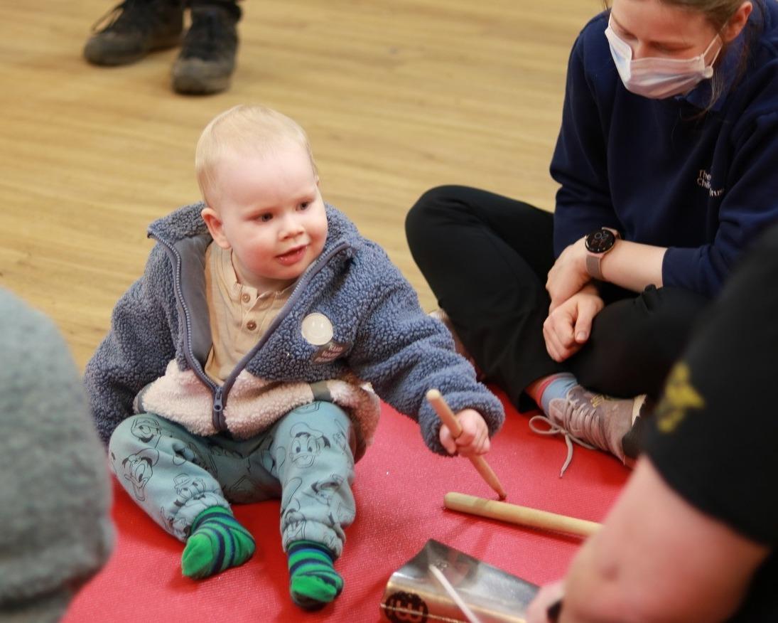 Isaac sitting up holding a drumstick and percussion instrument