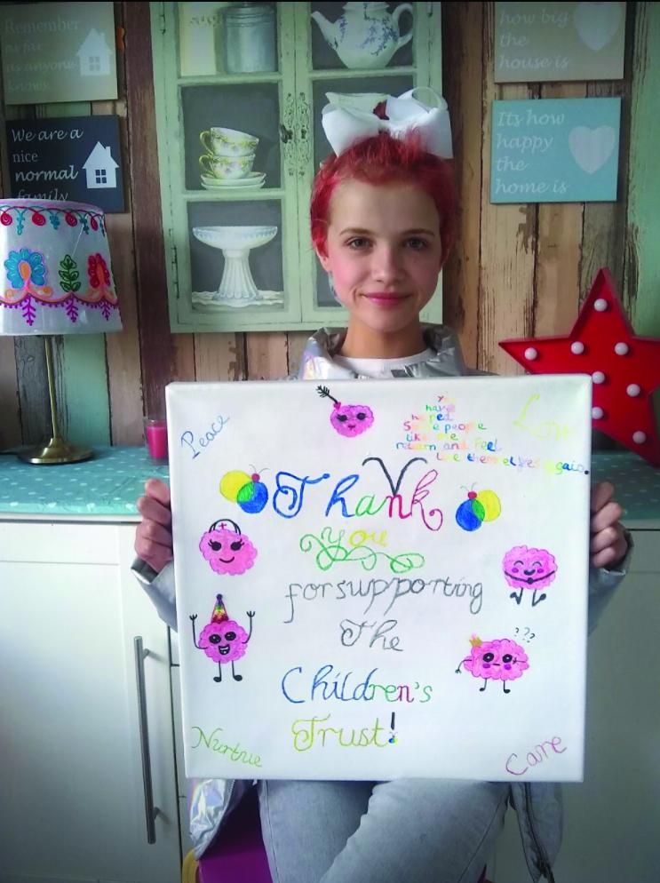 Mia holding a thank you card to The Children's Trust