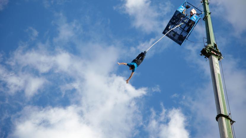person bungee jumping against blue sky backdrop with white clouds