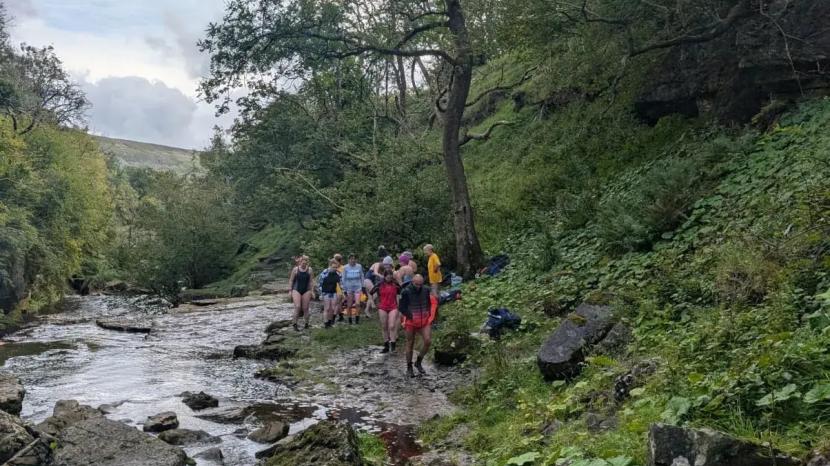 hikers along the side of a river running through a lush green mountainous valley